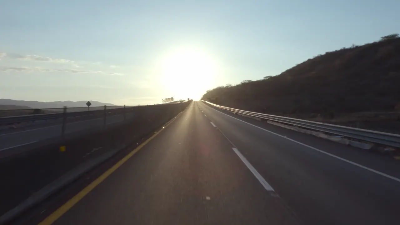 Vista do motorista numa estrada, dirigindo contra o sol